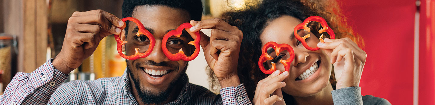 Two silly people holding slices bell peppers over their eyes