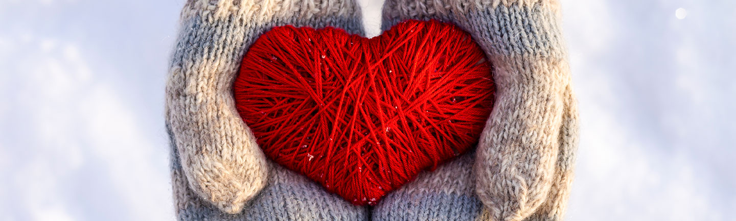 Photo of 2 hands with mittens on holding a red heart made of yarn