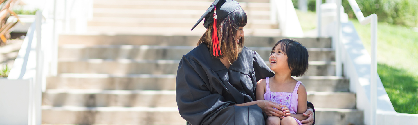A graduate sitting on a set of steps next to her daughter