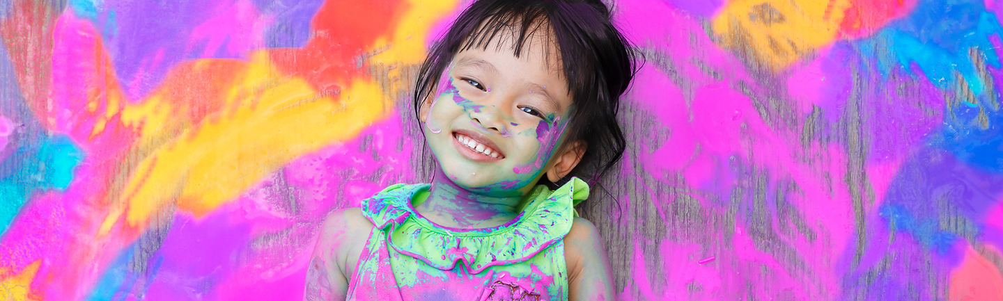 A happy child surrounded by colourful paint