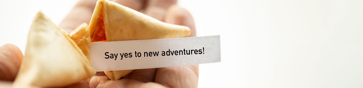 Person holding a fortune cookie that says "say yes to new adventures"