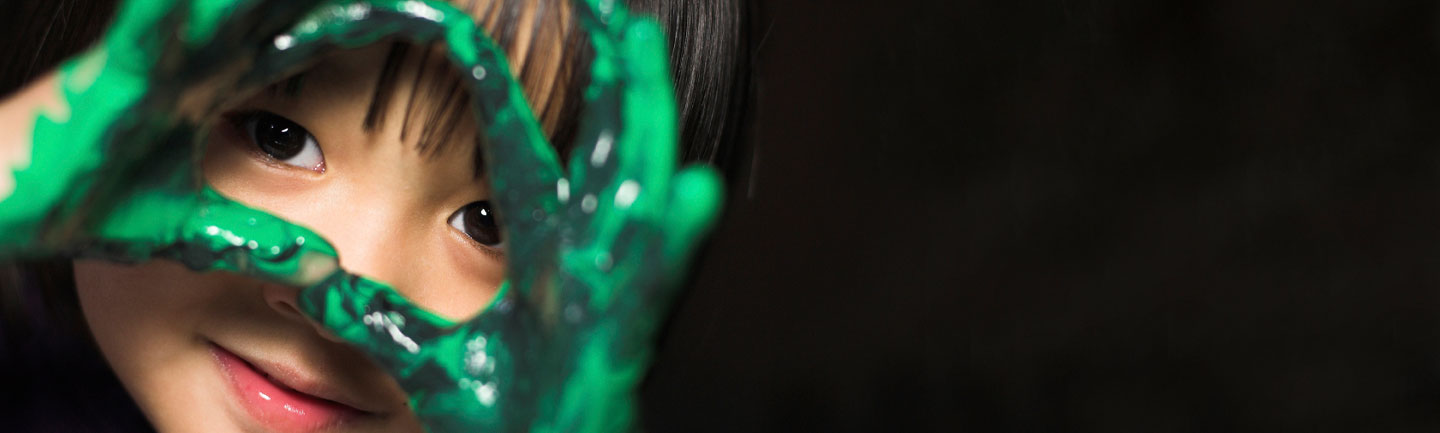 Child with paint on her hands against a black background