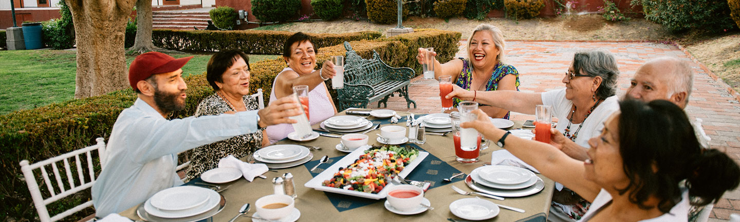 Photo of people sitting around a table eating food and raising their glasses in the air