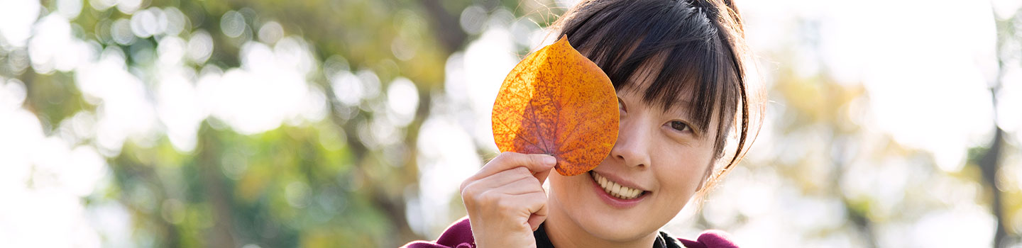 Photo of a woman holding an orange leaf in front of her face