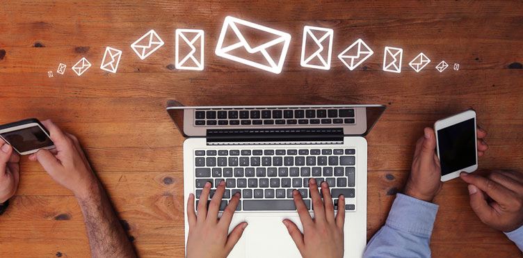 Photo of person typing on a laptop and another person on their cell phone