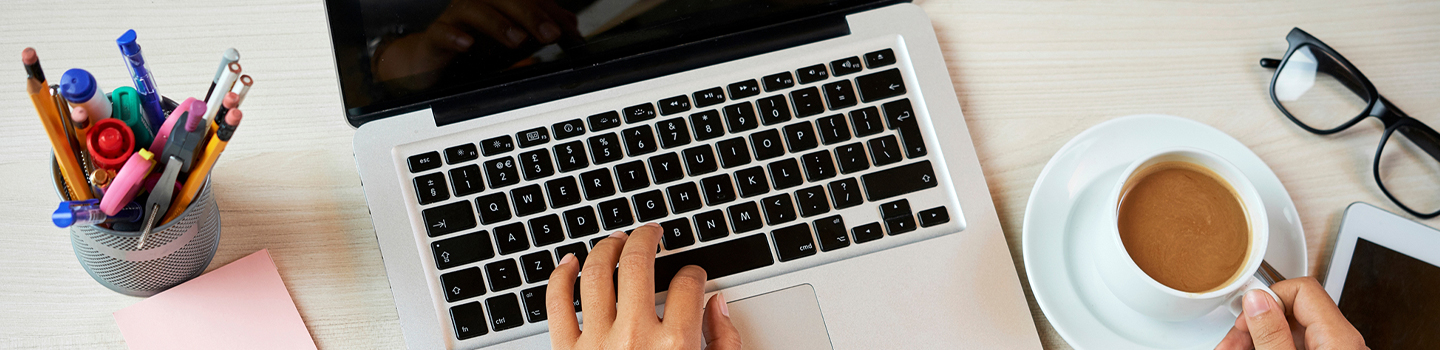 Photograph of a laptop with a cup of coffee beside it