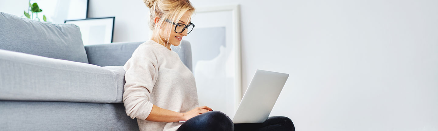 A young woman sitting against her couch with a laptop