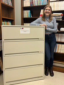 Mackenzie Smith (BA'22, MA’24) standing by the cabinets containing the Dr. Agatha Bonga Memorial Collection at the Gregg Centre for the Study of War and Society at UNB’s Fredericton campus.