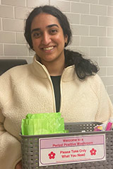 Photo of Sarah Mahood of the the UNB Saint John campus Menstrual Health Society with a basket of menstrual products.