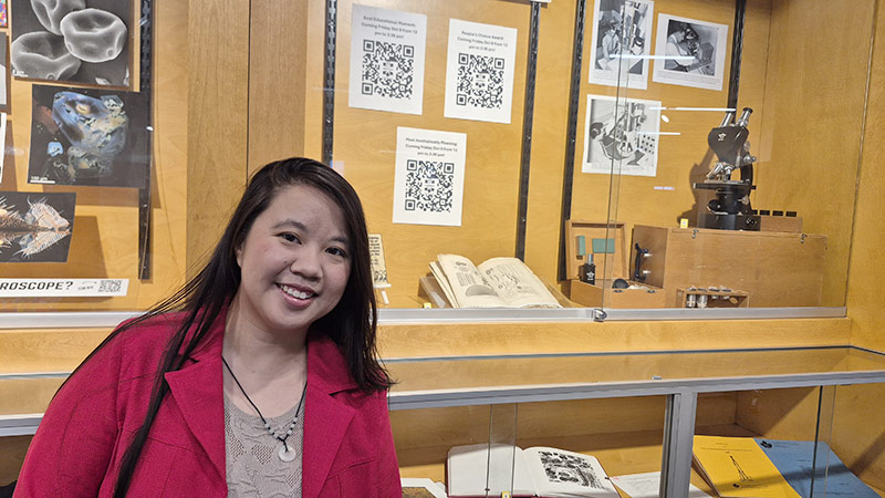 Nhu P. V. Trieu, the MMF’s Acting Director, standing by a display at the Harriet Irving Library celebrating the MMF’s 60th anniversary.